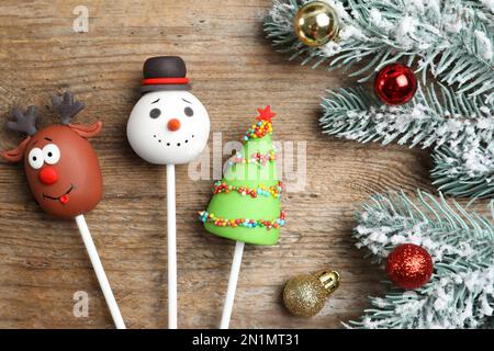 Délicieux gâteaux à thème de Noël et branches de sapin avec boules sur table en bois, plat Banque D'Images