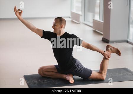 Un homme de construction athlétique fait du yoga dans la salle de gym sur un tapis. Banque D'Images