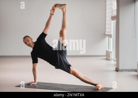 Un homme de construction athlétique fait du yoga dans la salle de gym sur un tapis. Banque D'Images