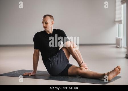 Un homme de construction athlétique fait du yoga dans la salle de gym sur un tapis. Banque D'Images