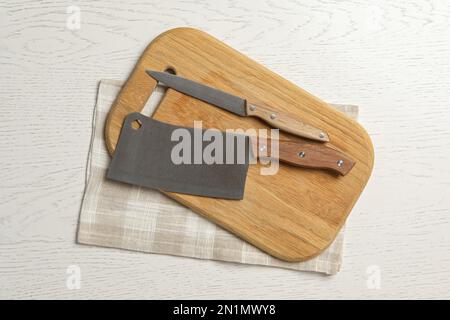 Couteaux, planche à découper et serviette sur fond de bois blanc, plat. Ustensiles de cuisine Banque D'Images