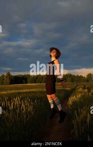 Une adolescente portant des chaussettes de genou avec des rayures arc-en-ciel saute haut dans l'air tournant son visage au soleil de mise en place Banque D'Images