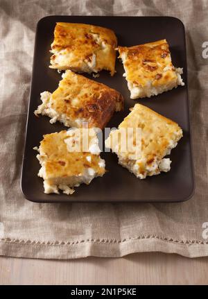 Tarte au fromage avec feta, sans croûte sur une assiette brune, torchon beige, table en bois. Une excellente idée pour la boîte à lunch. Banque D'Images