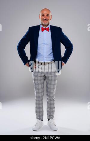 Prise de vue en studio d'un homme souriant portant un noeud papillon et un pantalon à carreaux sur fond gris isolé. Copier l'espace. Banque D'Images