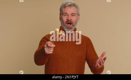 Magicien sorcière homme gestante avec baguette magique de fée, faire le désir de devenir vrai, casting magicien sort, publicité vacances vente rabais. Homme d'âge moyen isolé sur fond de studio beige Banque D'Images