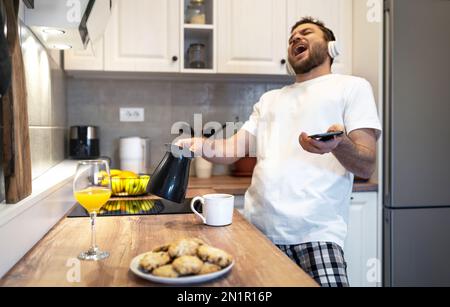 Homme dans un casque qui fait du café le matin en écoutant de la musique et en chantant seul. Banque D'Images