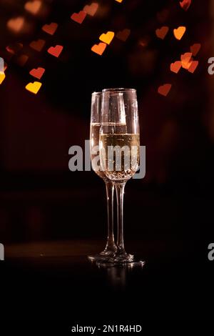 Deux verres de champagne, qui se tiennent sur un fond noir avec un beau bokeh, des verres contre le fond des coeurs, le concept de la Saint-Valentin, dîner romantique. Copier l'espace. Haute qualité Banque D'Images