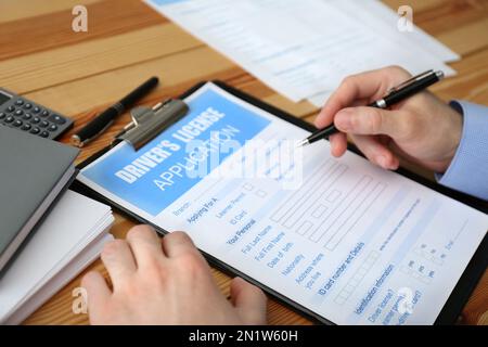 Homme remplissant le formulaire de demande de permis de conduire à une table en bois, en gros plan Banque D'Images