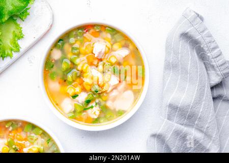 Soupe légère de légumes avec poulet, maïs et haricots verts. Cuisine de confort. Arrière-plan de table blanc, vue du dessus Banque D'Images