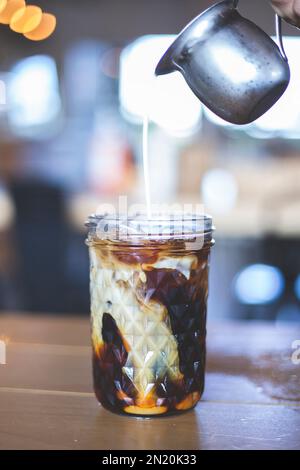 Café glacé dans un grand verre et crème versée. Café noir froid avec glaçons dans une crème à haute teneur en verre. Barista. Taille basse Banque D'Images