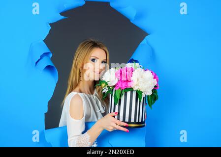 Femme avec bouquet de fleurs. Belle fille avec bouquet de pivoines. Fleurs présentes pour femme. Fille souriante avec bouquet de pivoines regardant à travers le papier Banque D'Images