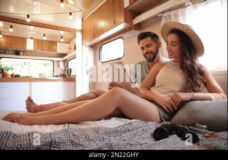 Un jeune couple heureux lisant le journal au lit dans une remorque. Vacances en camping Banque D'Images