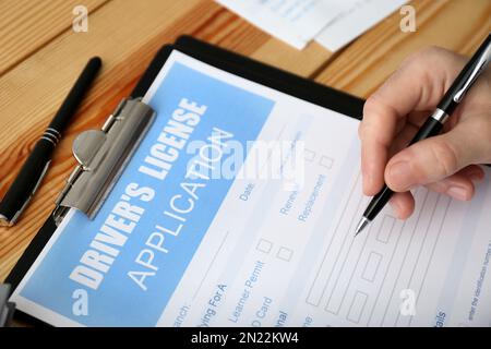 Homme remplissant le formulaire de demande de permis de conduire à une table en bois, en gros plan Banque D'Images