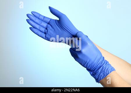 Femme mettant des gants en latex sur fond bleu clair, gros plan des mains Banque D'Images