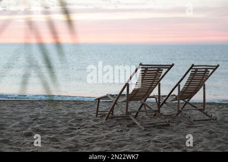 Chaises longues en bois sur la plage de sable au coucher du soleil. Vacances d'été Banque D'Images