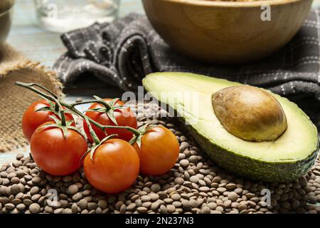 Les légumes sont encore vivants avec des tomates cerises de vigne et la moitié d'un avocat sur une feuille de lentilles séchées Banque D'Images