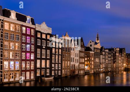 AMSTERDAM, PAYS-BAS - 18 JANVIER 2023 : paysage urbain de maisons hollandaises traditionnelles pendant l'heure bleue au canal de Damrak à Amsterdam Banque D'Images