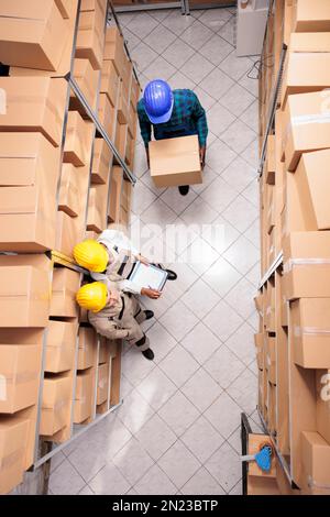 Employés d'entrepôt gérant la réception de colis, transportant une boîte en carton. Divers gestionnaires de magasins de détail, hommes et femmes, travaillant et coordonnant la chaîne d'approvisionnement des biens, vue du dessus Banque D'Images