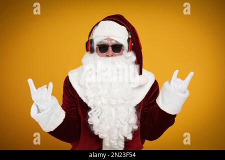 Le Père Noël est équipé d'un casque qui écoute la musique de Noël sur fond jaune Banque D'Images