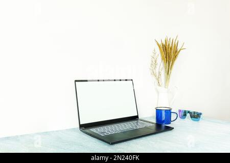 Image d'un ordinateur portable fin avec un écran vierge à côté d'une tasse de café, une tasse de métal décorative et des lunettes de soleil et un écran d'ordinateur avec les mêmes objets Banque D'Images