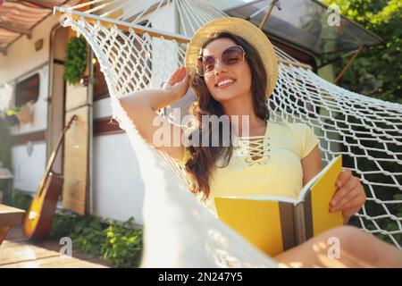 Jeune femme avec livre se reposant dans un hamac près de motorhome à l'extérieur le jour ensoleillé Banque D'Images