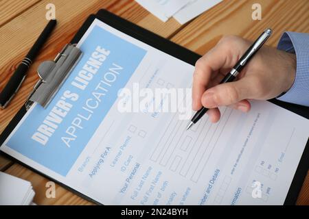 Homme remplissant le formulaire de demande de permis de conduire à une table en bois, en gros plan Banque D'Images