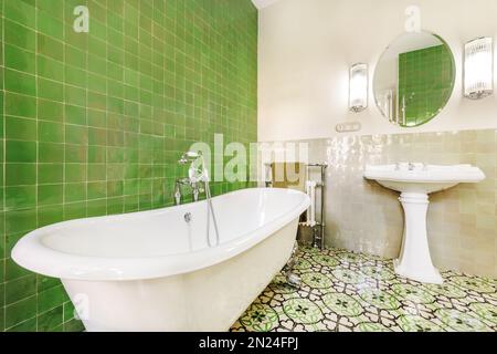 Belle salle de bains décorée dans un style vintage avec baignoire à griffes, carrelage hydraulique sur le sol et murs verts et évier en porcelaine blanche avec bevele circulaire Banque D'Images