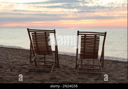 Chaises longues en bois sur la plage de sable au coucher du soleil. Vacances d'été Banque D'Images