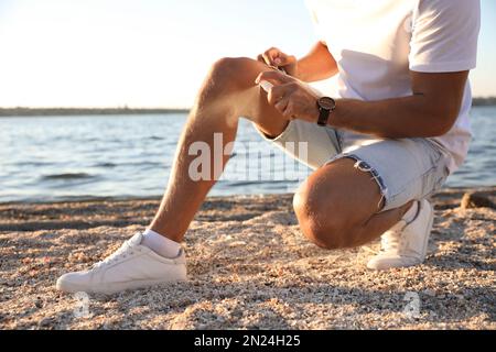 Homme utilisant un insectifuge près de la mer le jour ensoleillé, gros plan Banque D'Images