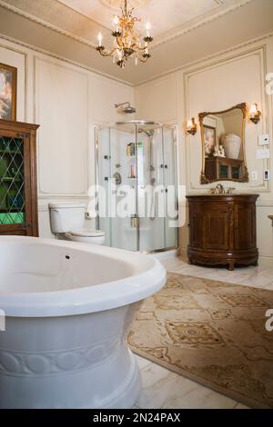 Baignoire autoportante de style bateau, cabine de douche en verre et meuble-lavabo en bois dans la salle de bains principale à l'étage à l'intérieur de la maison de style Renaissance. Banque D'Images