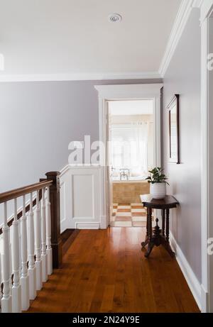 Main courante en bois brun avec broches blanches et couloir avec plancher en merisier menant à la salle de bains principale à l'étage à l'intérieur de la maison contemporaine. Banque D'Images