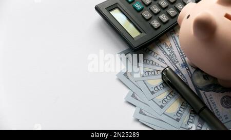 Une calculatrice, un stylo et une tirelire sur un dollar ou des billets de banque sur fond blanc avec un espace de copie. Banque D'Images