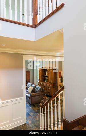 Vue sur le salon avec canapé en cuir brun et buffet depuis les escaliers en merisier à l'intérieur de la maison de style cottage contemporain. Banque D'Images