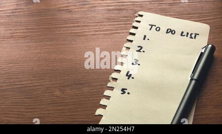 Une liste de tâches écrites sur un morceau de papier avec un stylo sur fond en bois avec un espace de copie. Banque D'Images