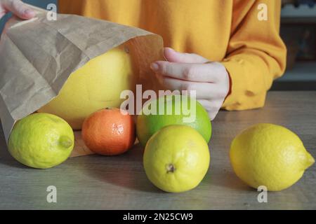 Une femme dans un chandail jaune prend un fruit aux couleurs vives d'un sac en papier gros plan Banque D'Images