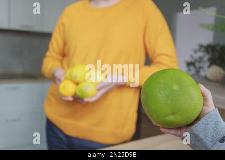 La main d'un enfant tient un pamplemousse vert en gros plan sur le fond d'une silhouette masculine dans un chandail jaune dont les mains sont de cinq citrons Banque D'Images