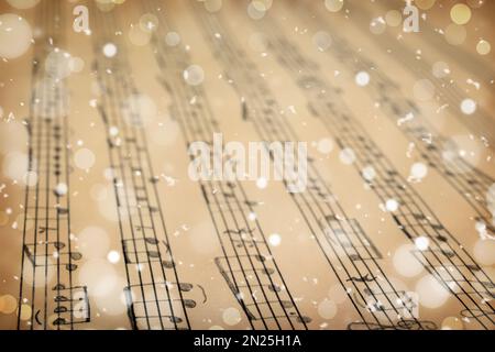 Feuille ancienne avec notes de musique de Noël comme fond, flocons de neige et effet bokeh Banque D'Images