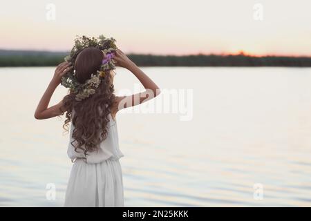 Petite fille portant une couronne faite de belles fleurs près de la rivière au coucher du soleil Banque D'Images