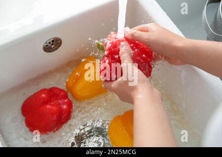 Femme lavant des poivrons frais dans l'évier de cuisine, gros plan Banque D'Images