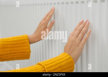 Femme se réchauffant les mains sur le radiateur de chauffage, gros plan Banque D'Images