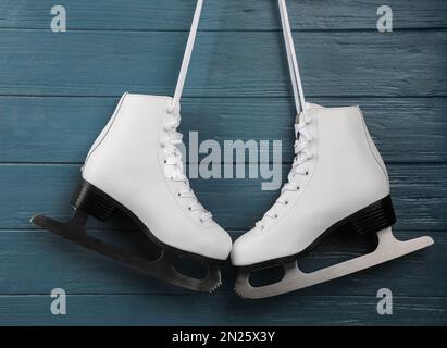 Paire de patins à glace blancs suspendus sur fond en bois bleu Banque D'Images