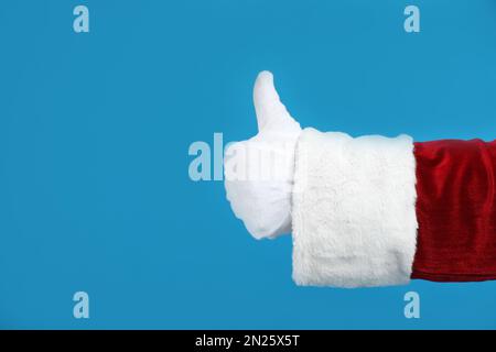 Père Noël montrant le pouce vers le haut sur fond bleu, gros plan de la main Banque D'Images