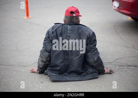 L'homme sans abri est assis sur la route. Un homme sans logement est assis sur le trottoir. L'homme a perdu la capacité de marcher. Le vieil homme pauvre attend de l'aide. Banque D'Images