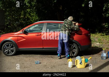 L'homme lave la voiture rouge. Le retraité lave la voiture. Travailler avec le transport. Détergents près de la voiture. Banque D'Images