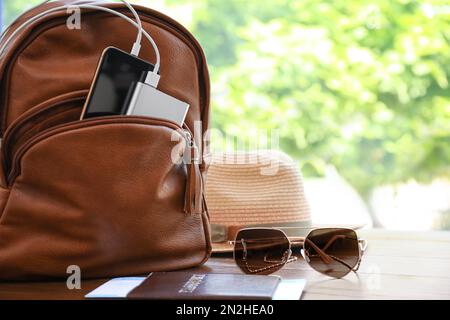 Lunettes de soleil, passeport, chapeau et sac à dos avec gadgets sur table en bois, espace pour le texte. Chargement des composants électroniques pendant le déplacement Banque D'Images