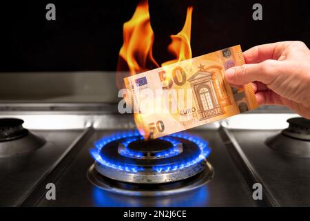 Un homme brûle une note de 50 euros au-dessus d'une flamme de gaz tout en la tenant dans sa main. Un billet de 50 euros brûle sur un poêle à gaz éclairé.concept sur le coût élevé du gaz. Banque D'Images