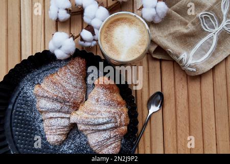 Croissants à croûte française, verre de Latte à l'extérieur. Un moment agréable. Fond pastel et décoration en coton. Banque D'Images