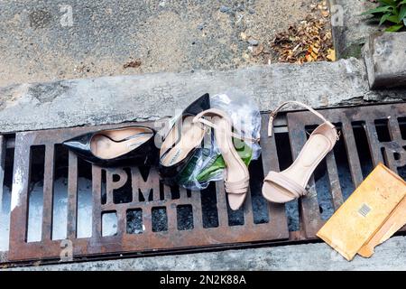 Deux paires de chaussures jetées et cassées pour femmes sur un drain à Ho Chi Minh ville, Vietnam Banque D'Images