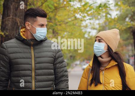 Couple dans les masques médicaux de visage marchant à l'extérieur. Protection personnelle pendant la pandémie de COVID-19 Banque D'Images