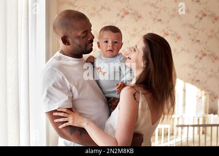 Famille heureuse avec bébé à la maison. Portrait de maman et de papa tenant le bébé de leur fils dans leurs bras, souriant. Mère et Père amoureux Banque D'Images